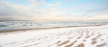 Gün batımında karla kaplı Baltık deniz kıyısından bir manzara. Riga Körfezi, Letonya. Renkli dramatik bulut manzarası. Kararsız hava, dalgalar ve su sıçramaları. Kış turizmi, küresel ısınma teması