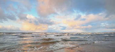 Baltık Denizi 'nin üzerindeki renkli günbatımı bulutları, kışın kasırga. Dramatik gökyüzü, dalgalar ve su sıçramaları. Ekoloji, iklim değişikliği, küresel ısınma kavramları