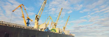 Gün batımında limana demir atmış büyük bir kargo gemisi. Vinçler arka planda. Riga, Baltık Denizi, Letonya. Yük taşımacılığı, küresel iletişim, lojistik, çevresel hasar