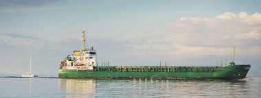 Büyük yeşil kargo gemisi ve beyaz yelkenli (katamaran) gün batımında açık bir Karayip Denizi 'nde yol alırlar. Görüntüyü algıla. Nakliye, endüstri, küresel iletişim, lojistik, spor, eğlence