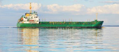 Büyük yeşil kargo gemisi gün batımında açık denizde yelken açıyor. Renkli parlayan bulutlar, sıcak güneş ışığı. Görüntüyü algıla. Nakliye, iş, ekonomi, sanayi, küresel iletişim, lojistik