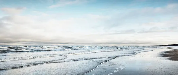 日没時には雪に覆われたバルト海の海岸からの眺め ラトビアのリガ湾 劇的な空だ クリスタルクリアブルー水 ひどい天気 波と水が飛び散った 冬の観光 地球温暖化のテーマ — ストック写真