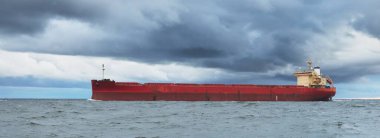 Büyük kırmızı kargo gemisi karanlık günbatımı göğünün altında açık denizde yol alıyor. Southampton 'da. İngiltere. Dramatik bulutlar, kasırga, fırtınalı hava. Küresel iletişim, nakliye, endüstri, lojistik