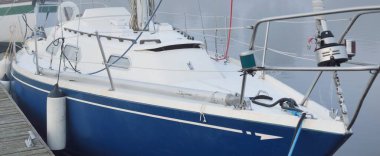 Mavi şalopa donanımlı yat, güneşin doğuşunda yoğun beyaz bir sabah sisinde bir iskeleye demirlemiş. Kiel, Almanya 'daki yat kulübü. Spor, eğlence, ulaşım teması