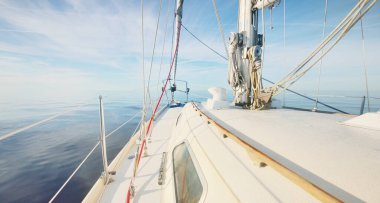 Durgun bir yaz gününde, durgun bir suda yüzen beyaz bir yat. Güverteden pruvaya, direğe ve yelkenlere yakın görüntü. Sudaki yansımalar. Idyllic deniz manzarası. Ruhnu Adası, Estonya, Baltık Denizi