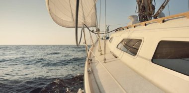 Gün batımında açık denizde yelkenli yelkenli yelkenli. Gökyüzü açık. Güverteden pruvaya bir manzara, direk, yelkenler. Ulaşım, seyahat, gezi, spor, eğlence, boş zaman aktivitesi, yarış, yelkenli yarışı