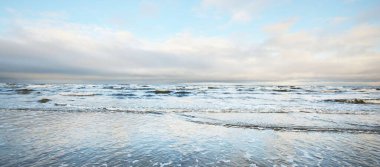 Gün batımında karla kaplı Baltık deniz kıyısından bir manzara. Riga Körfezi, Letonya. Dramatik bir gökyüzü. Kristal berrak mavi su. Kararsız hava, dalgalar ve su sıçramaları. Kış turizmi, küresel ısınma teması