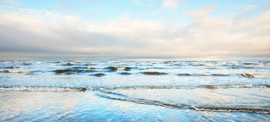 Gün batımında karla kaplı Baltık deniz kıyısından bir manzara. Riga Körfezi, Letonya. Dramatik bir gökyüzü. Kristal berrak mavi su. Kararsız hava, dalgalar ve su sıçramaları. Kış turizmi, küresel ısınma teması