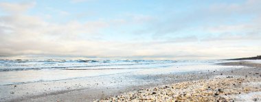 Bir sürü deniz kabuğuyla kaplı Baltık deniz kıyısından bir manzara. Riga Körfezi, Letonya. Renkli dramatik bulut manzarası. Kararsız hava, dalgalar, su sıçramaları. Kış turizmi, küresel ısınma