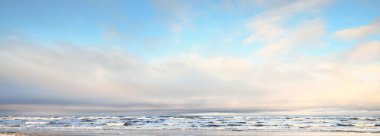 Gün batımında karla kaplı Baltık deniz kıyısından bir manzara. Riga Körfezi, Letonya. Renkli dramatik bulut manzarası. Kararsız hava, dalgalar ve su sıçramaları. Kış turizmi, küresel ısınma teması