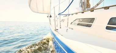 Güneşli bir yaz gününde beyaz bir yat denize açılıyor. Güverteden pruva ve yelkenlere kadar yakın çekim. Dalgalar ve su sıçramaları. Açık mavi gökyüzü. Baltık Denizi, İsveç