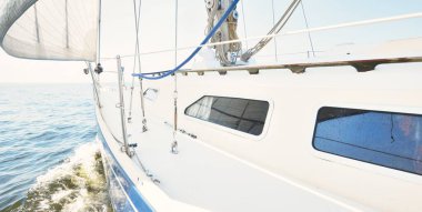 Güneşli bir yaz gününde beyaz bir yat denize açılıyor. Güverteden pruva ve yelkenlere kadar yakın çekim. Dalgalar ve su sıçramaları. Açık mavi gökyüzü. Baltık Denizi, İsveç