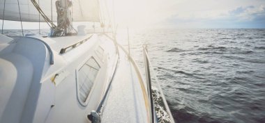 Beyaz yat gün batımında açık denizde yüzüyor. Güverteden pruva ve yelkenlere kadar yakın çekim. Fırtınadan sonra renkli bulutlarla dramatik bir gökyüzü. Dalgalar ve su sıçrıyor. Spor ve eğlence teması