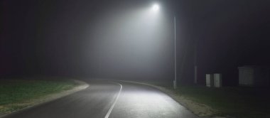 Gece sisli ve keskin bir dönüş yapan boş bir otoyol. Yol tabelası yakın plan. Karanlık şehir manzarası, şehir manzarası. Riga, Letonya. Tehlikeli sürüş, hız, özgürlük, konsept görüntü