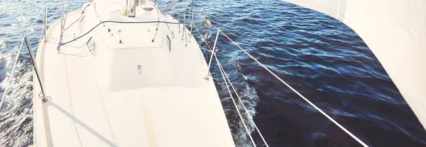 A couple of people on the white yacht sailing on a clear day. Top down view from the bow to the deck, mast and sails. Recreation and summer sport theme. Ruhnu island, Estonia