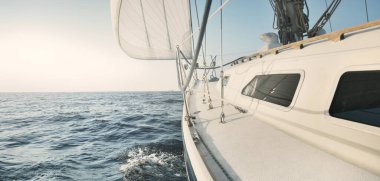 Gün batımında açık denizde yelkenli yelkenli yelkenli. Gökyüzü açık. Güverteden pruvaya bir manzara, direk, yelkenler. Ulaşım, seyahat, gezi, spor, eğlence, boş zaman aktivitesi, yarış, yelkenli yarışı