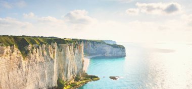 Gün batımında Etretat beyaz uçurumlarının manzaralı panoramik görüntüsü. Dramatik gökyüzü, gök mavisi su. Fransa, Normandiya 'da yaz tatili. Seyahat yerleri, ulusal dönüm noktaları, geziler, tarih.