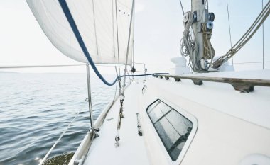 Güneşli bir yaz gününde beyaz bir yat denize açılıyor. Güverteden pruva ve yelkenlere kadar yakın çekim. Dalgalar ve su sıçramaları. Açık mavi gökyüzü. Baltık Denizi, İsveç