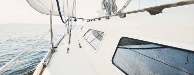 Güneşli bir yaz gününde beyaz bir yat denize açılıyor. Güverteden pruva ve yelkenlere kadar yakın çekim. Dalgalar ve su sıçramaları. Açık mavi gökyüzü. Baltık Denizi, İsveç