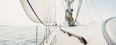 Güneşli bir yaz gününde beyaz bir yat denize açılıyor. Güverteden pruva ve yelkenlere kadar yakın çekim. Dalgalar ve su sıçramaları. Açık mavi gökyüzü. Baltık Denizi, İsveç