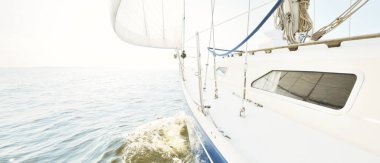 Güneşli bir yaz gününde beyaz bir yat denize açılıyor. Güverteden pruva ve yelkenlere kadar yakın çekim. Dalgalar ve su sıçramaları. Açık mavi gökyüzü. Baltık Denizi, İsveç