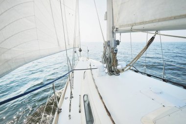 Güneşli bir yaz gününde beyaz bir yat denize açılıyor. Güverteden pruva ve yelkenlere kadar yukarıdan aşağıya doğru. Dalgalar ve su sıçramaları. Açık mavi gökyüzü. Baltık Denizi, İsveç