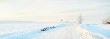 Gün batımında kar fırtınasından sonra karla kaplı arazide köy yolu. Gökyüzü açık, altın ışık. Idyllic kırsal kesim. Panoramik manzara. Noel, lojistik, tehlikeli sürüş, off-road, ulaşım