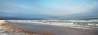 Gün batımında karla kaplı Baltık deniz kıyısından bir manzara. Riga Körfezi, Letonya. Dramatik mavi gökyüzü. Kararsız hava, dalgalar ve su sıçramaları. Kış turizmi, küresel ısınma teması