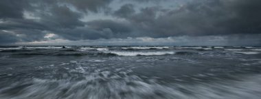 Baltık Denizi 'nin üzerinde kara fırtına var, dalgalar ve su fışkırıyor. Dramatik bulut manzarası. Doğa, çevre, kararsız hava, iklim değişikliği. Atmosferik manzara. Panoramik görünüm, uzun pozlama