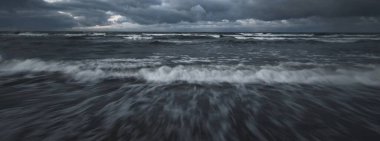 Kışın Baltık Denizi 'nin üzerindeki fırtına bulutları, uzun pozlama. Dramatik günbatımı gökyüzü, dalgalar ve su sıçramaları. Koyu deniz manzarası. Almanya