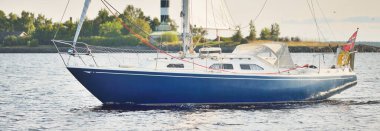 Gün batımında Riga körfezinde mavi yelkenli yelkenli yelkenli. Yakın plan. Baltık Denizi, Letonya. Arka planda deniz feneri var. Yarış, spor, eğlence, eğlence aktivitesi, takım çalışması kavramları.