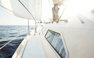 Gün batımında açık denizde yelkenli yelkenli yelkenli. Gökyüzü açık. Güverteden pruvaya bir manzara, direk, yelkenler. Ulaşım, seyahat, gezi, spor, eğlence, boş zaman aktivitesi, yarış, yelkenli yarışı