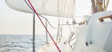 Gün batımında açık denizde yelkenli yelkenli yelkenli. Gökyüzü açık. Güverteden pruvaya bir manzara, direk, yelkenler. Ulaşım, seyahat, gezi, spor, eğlence, boş zaman aktivitesi, yarış, yelkenli yarışı