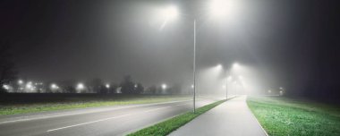 Gece sisli bir havada karayolu yakınında boş bir bisiklet yolu. Fenerler yakın plan. Ulaşım, tehlikeli sürüş, eğlence ve sağlıklı yaşam tarzı teması. Riga, Letonya