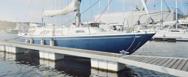 Zarif ve modern yelkenli tekneler (kiralık) açık bir günde yat limanındaki bir rıhtıma demirlediler. İsveç. Mavi şalopa donanımlı yat yakın plan. Tatiller, spor, amatör eğlence yelkenciliği, gemi yolculuğu.