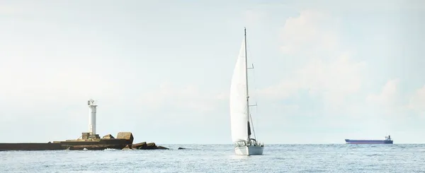 Small yacht sailing near the lighthouse on a clear day. Riga bay, Baltic sea, Latvia. Cruise, sport, recreation, leisure activity concepts