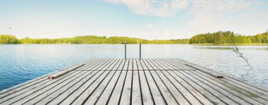Nehrin yakınındaki ahşap iskele. Arka planda Evergreen kozalaklı orman var. Açık mavi gökyüzü, suda yansımalar. Idyllic yaz manzarası. Eko turizm, eğlence teması. Finlandiya