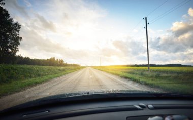 Yağmurdan sonra tarlalardan geçen boş bir köy yolu. Dramatik gökyüzü, destansı bulutlar. Arabadan bir manzara. Hava kararsız. - Letonya. Kasırga, fırtına, meteoroloji, ekoloji, doğal olaylar