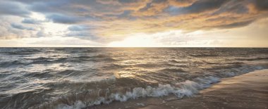 Gün batımında fırtınadan sonra Baltık Denizi kıyısında bir sürü koyu renkli kümülüs bulutu olan açık bir gökyüzü. Dramatik bulut manzarası. Sıcak altın ışık. Resimli bir manzara var. Kararsız hava, iklim değişikliği