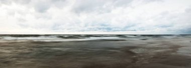 Fırtınadan sonra Baltık kıyıları. Dramatik günbatımı gökyüzü, karanlık parlayan bulutlar, altın güneş ışığı. Dalgalar, su sıçratma. Resimli manzara, deniz manzarası, bulut manzarası, doğa. Panoramik görünüm, uzun pozlama