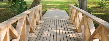 Açık bir günde yeşil yaprak döken ormanda modern ahşap patika (tahta yol), renkli akçaağaç yaprakları yakın çekim yapar. Güneş ışığı ve gölgeler. Eğlence, çevre, eko turizm, Letonya 'da tatiller