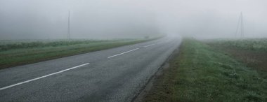 Gün doğumunda yoğun bir sis altında tarlalar ve ormanın içinden (asfalt yol) boş bir otoyol. Atmosferik manzara. Idyllic kırsal kesim. Karanlık, sonbahar mevsimi, kararsız hava, tehlikeli sürüş, yolculuk