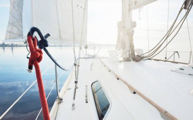Yağmurdan sonra beyaz yat yola çıkıyor. Güverteden pruvaya kadar yakın çekim. Durgun bir suya yansıyan açık mavi gökyüzü ve bulutlar. Doğal ayna. Idyllic deniz manzarası. Deniz, seyahat, seyahat yerleri;