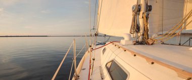 Günbatımında yağmurdan sonra beyaz yat denize açılacak. Güverteden pruvaya kadar yakın çekim. Durgun bir suya yansıyan parlak bulutlarla dolu berrak mavi bir gökyüzü. Idyllic deniz manzarası. Deniz, seyahat, seyahat yerleri