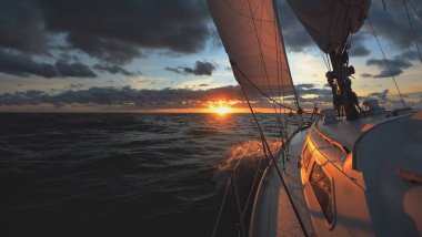 Gün batımında açık denizde yelken açmak. Güvertenin yakın görüntüsü, direk ve yelkenler. Yağmurdan sonra açık gökyüzü, çarpıcı parlayan bulutlar, altın güneş ışığı, dalgalar ve su sıçramaları, kasırga. Destansı deniz manzarası