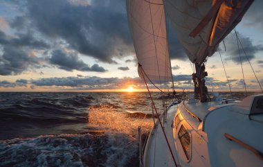 Gün batımında açık denizde yelken açmak. Güvertenin yakın görüntüsü, direk ve yelkenler. Yağmurdan sonra açık gökyüzü, çarpıcı parlayan bulutlar, altın güneş ışığı, dalgalar ve su sıçramaları, kasırga. Destansı deniz manzarası