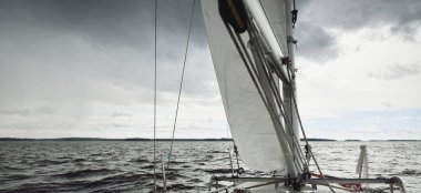 Fırtınada beyaz yat denize açılıyor. Direk görüntüsü, yelkenler, donanım. 9 metre İsviçre yapımı seyyar yelkenli. Yaz tatilleri, dinlenme, spor, boş zaman aktiviteleri.