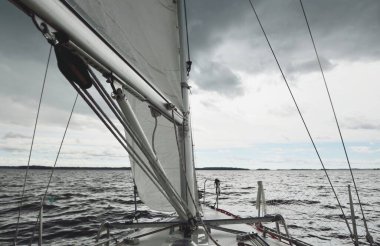 Fırtınada beyaz yat denize açılıyor. Direk görüntüsü, yelkenler, donanım. 9 metre İsviçre yapımı seyyar yelkenli. Yaz tatilleri, dinlenme, spor, boş zaman aktiviteleri.