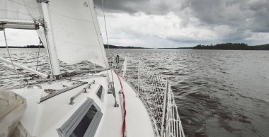 Fırtınada beyaz yat denize açılıyor. Direk görüntüsü, yelkenler, donanım. 9 metre İsviçre yapımı seyyar yelkenli. Yaz tatilleri, dinlenme, spor, boş zaman aktiviteleri.