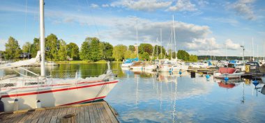 Klasik ve modern yelkenliler yat limanındaki bir rıhtıma demirlediler. Orman göl kıyısı. Yaz tatilleri, turizm, yat, dinlenme, spor, boş zaman aktiviteleri, yaşam tarzı.